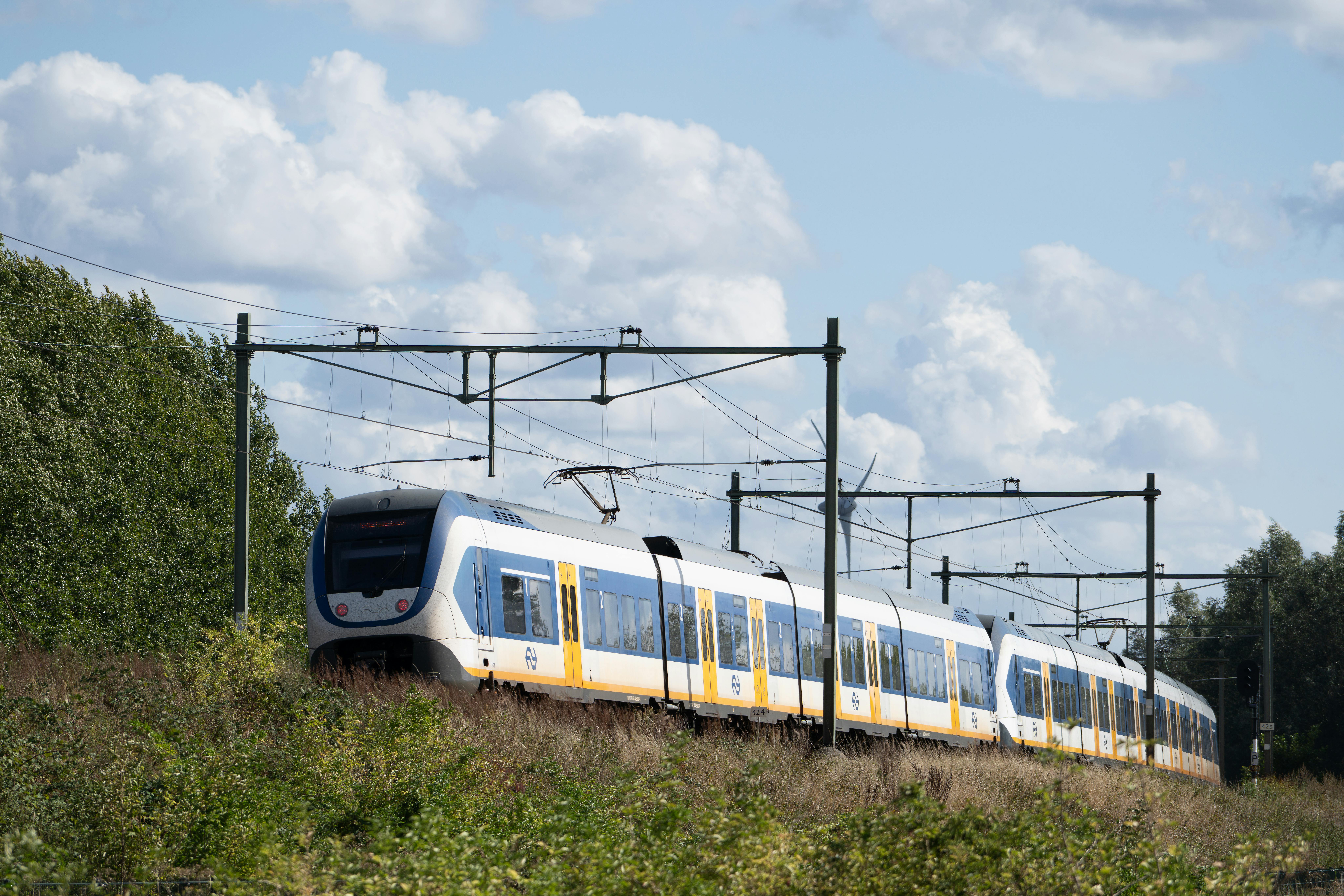 A modern electric train passes through lush countryside on a sunny day, showcasing efficient transportation.