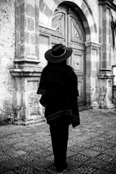 A person in traditional clothing stands before a historical door in Arequipa, Peru.