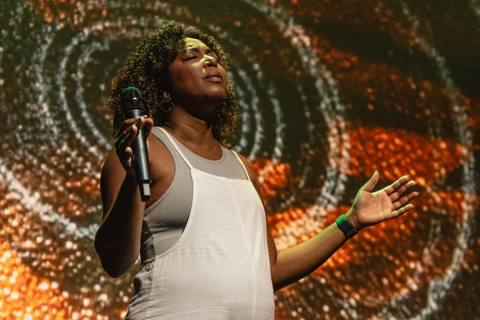 Female singer performing passionately with abstract spiral background on stage.