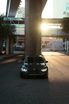 Modern black car parked under a bridge with the sun setting in the background.