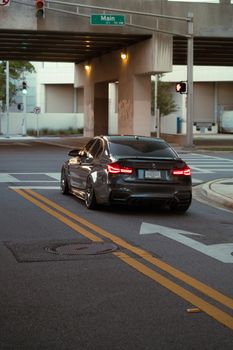 Sleek black luxury car driving through an urban street under a bridge during twilight.