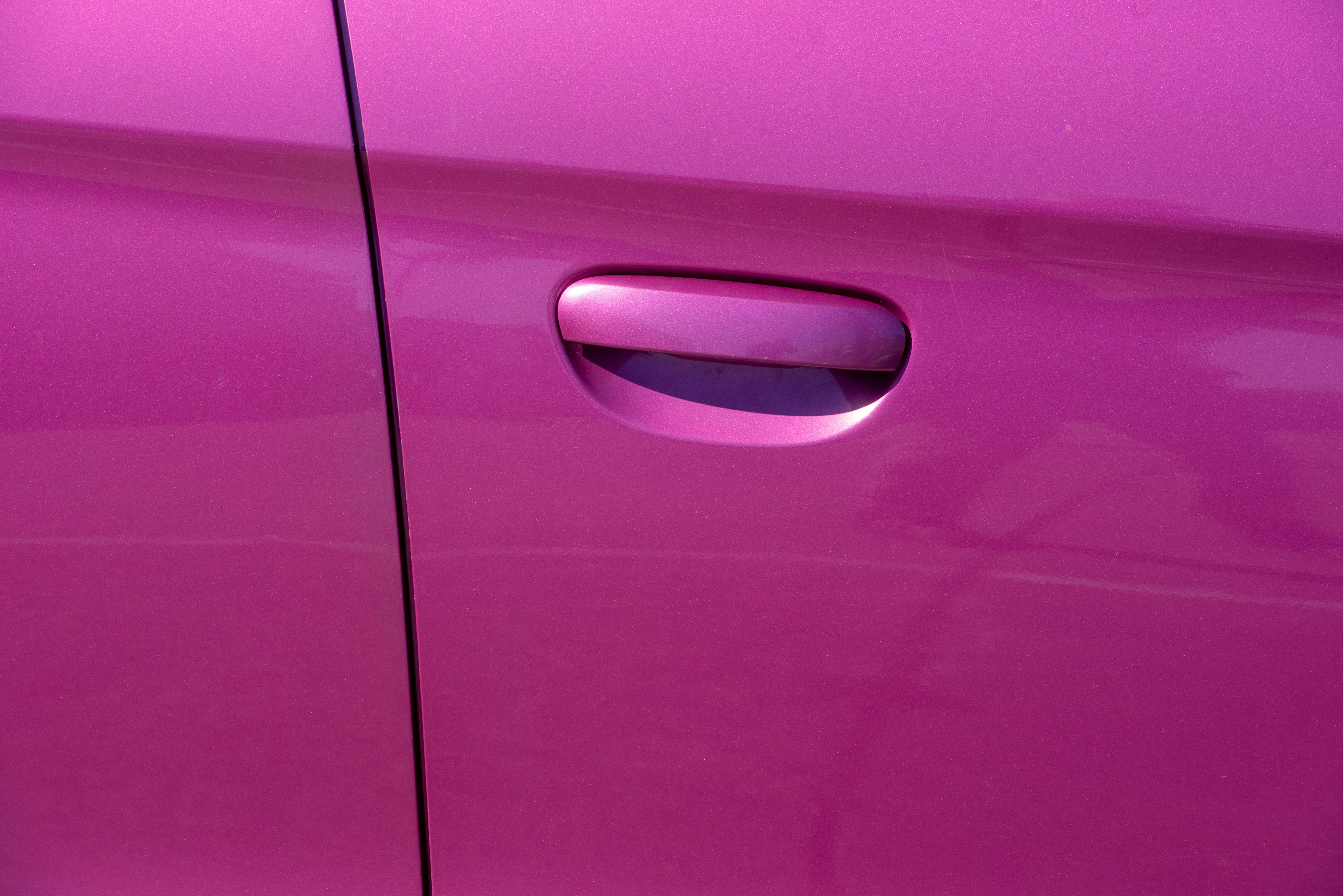 Close-up photograph of a vibrant pink car door handle, showcasing modern car design.