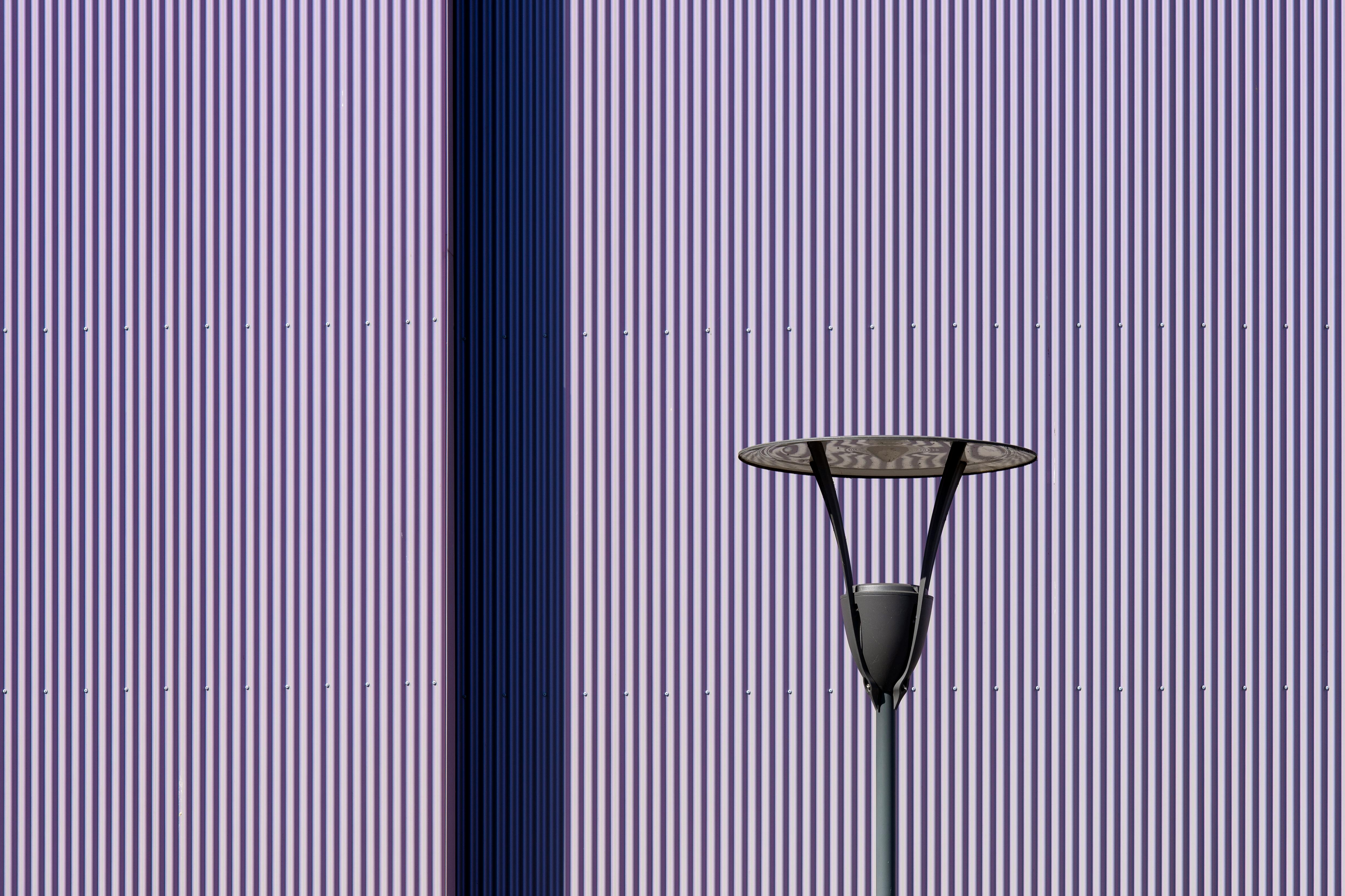 gratis Artistieke foto van een moderne lamp tegen een paars gestreepte muur, waardoor een minimalistische look ontstaat. Stockfoto
