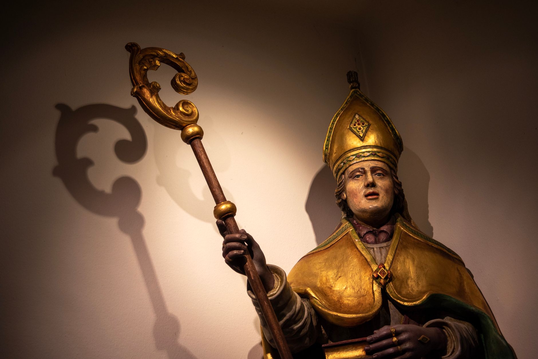 Illuminated statue of a bishop with a shadow cast on the wall in Holset, Limburg.