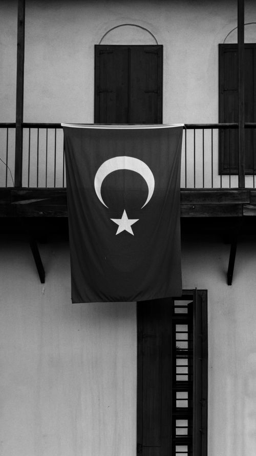 Free A black and white image of the Turkish flag hanging from a historic balcony, evoking timeless elegance. Stock Photo