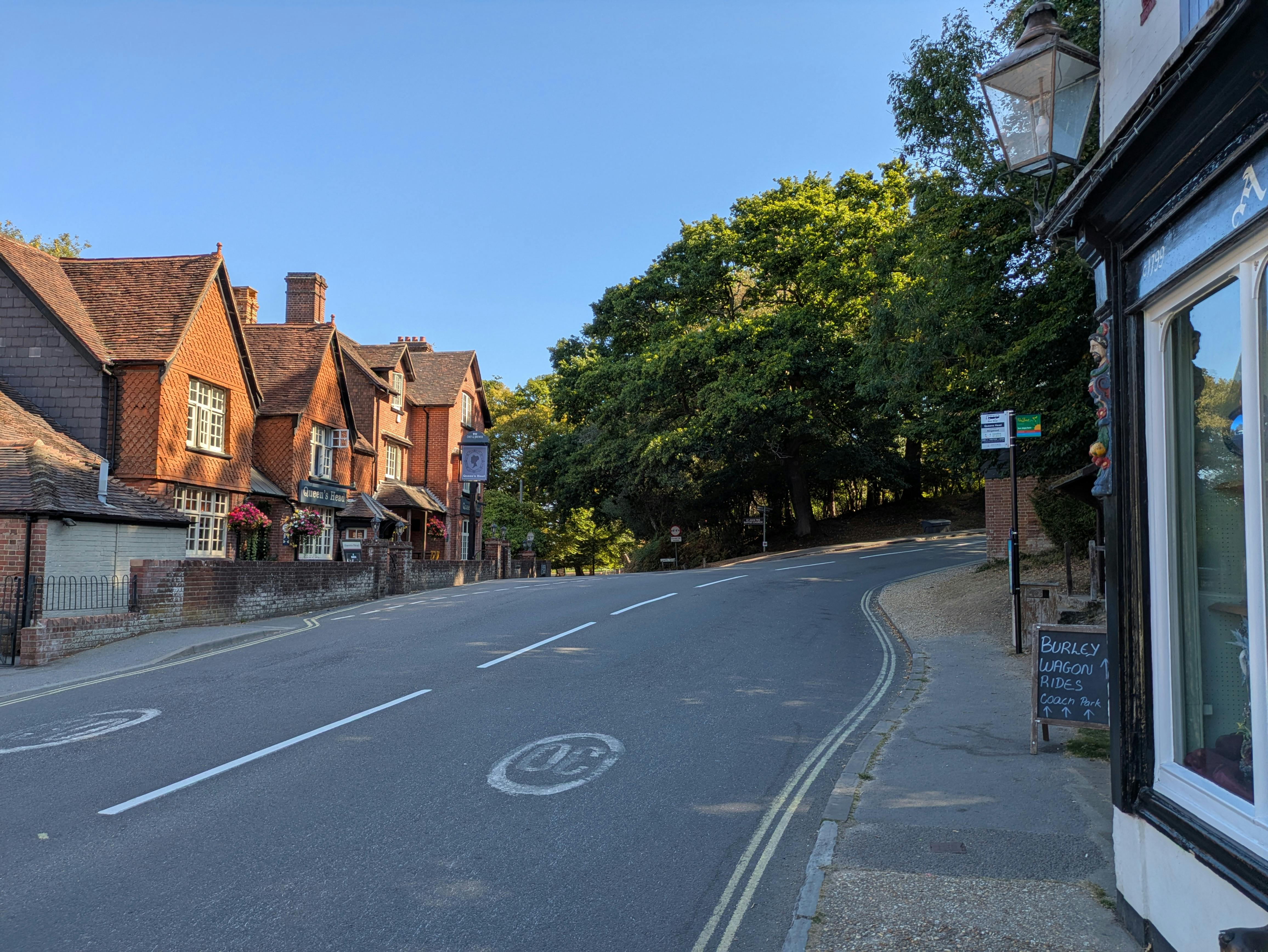 Picturesque street in a British village with brick houses and lush greenery in summer sunlight.