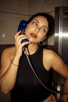 Woman using a retro blue telephone in an indoor booth, looking thoughtful.