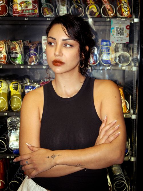 Free Young woman with tattoos stands confidently in front of a vending machine. Indoor setting, casual mood. Stock Photo