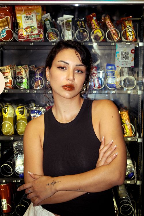 Free Young woman poses confidently against a vending machine stocked with snacks and drinks. Stock Photo