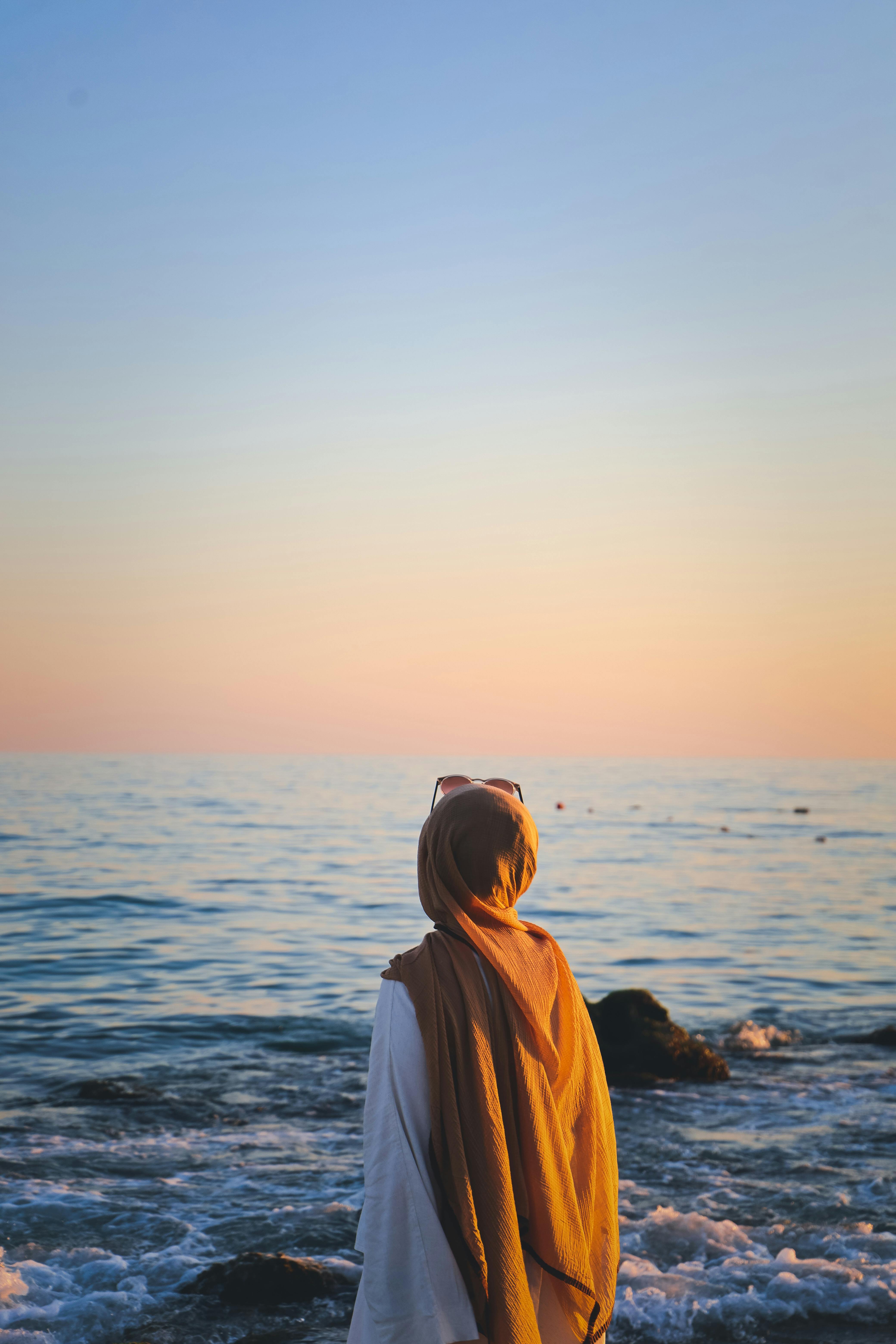 A woman in a hijab stands by the sea at sunset in Antalya, Türkiye.
