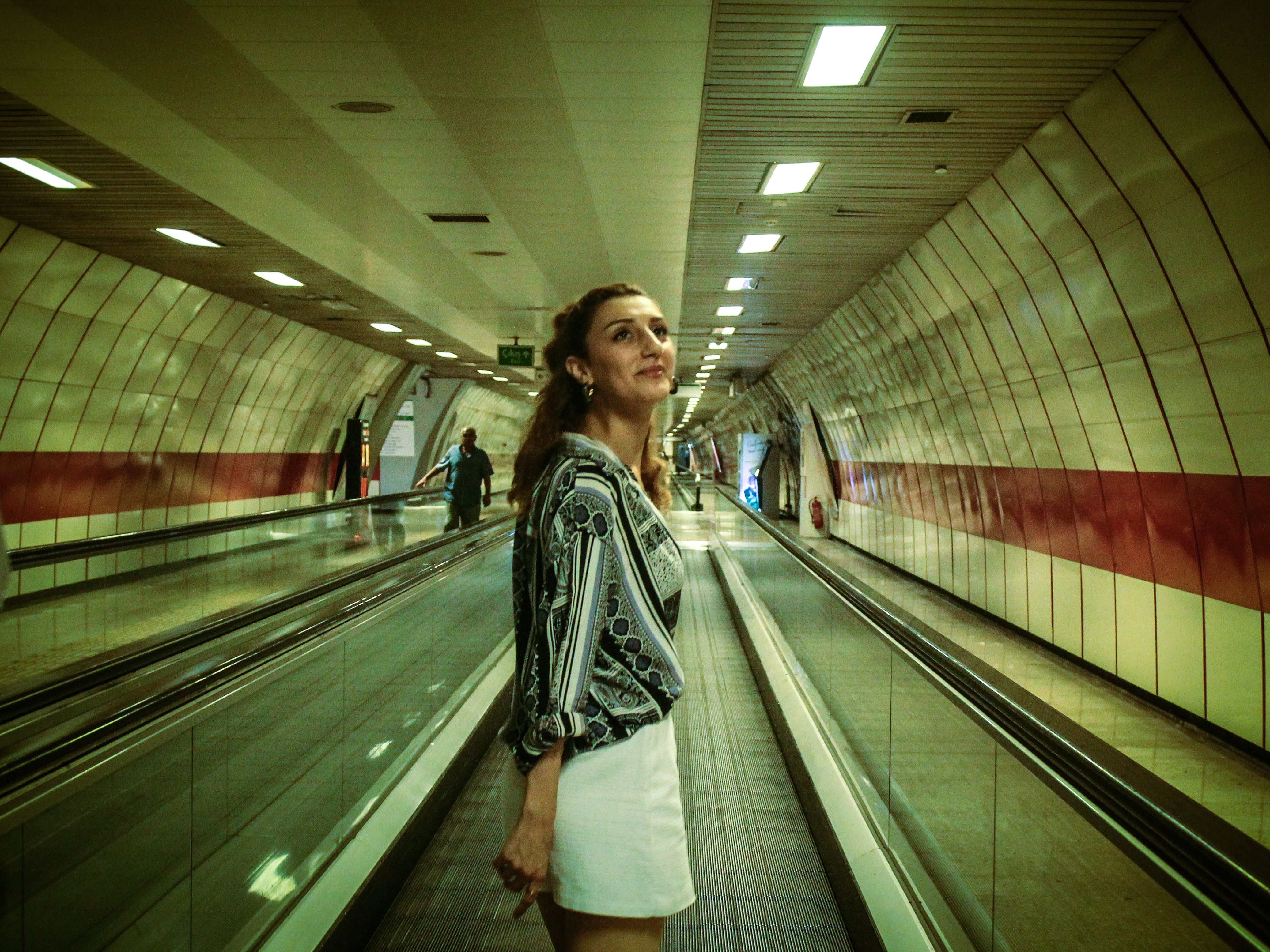 A woman in fashionable attire walks through a modern underground station.