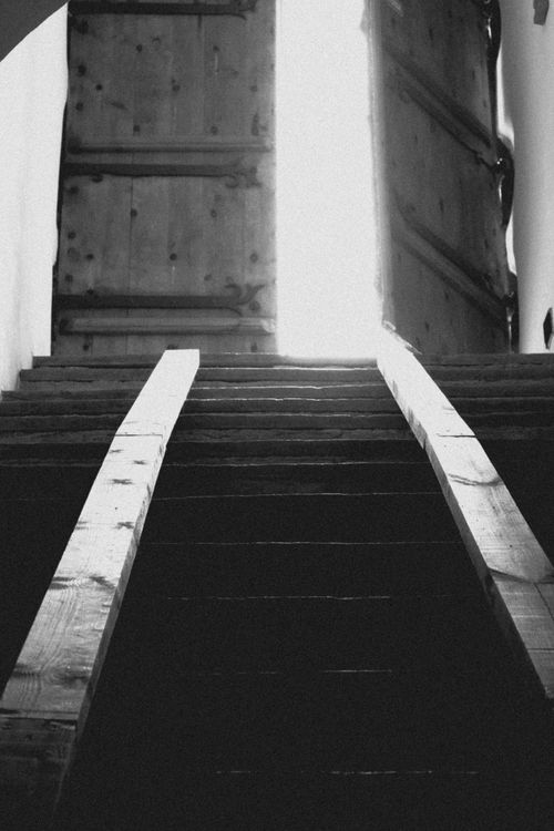 Free A black and white photo of an ancient wooden stairway leading to a bright open door. Stock Photo