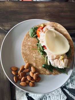 Nutritious chicken wrap with fresh vegetables and almonds on a plate.