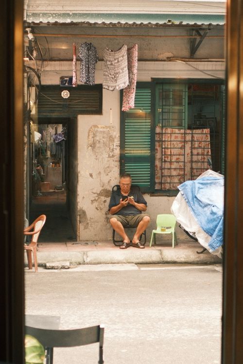 Free Elderly man on Jakarta street engrossed in his mobile phone, with traditional shophouse backdrop. Stock Photo