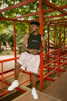 Young man in casual attire posing on a red bridge in a green urban park setting.