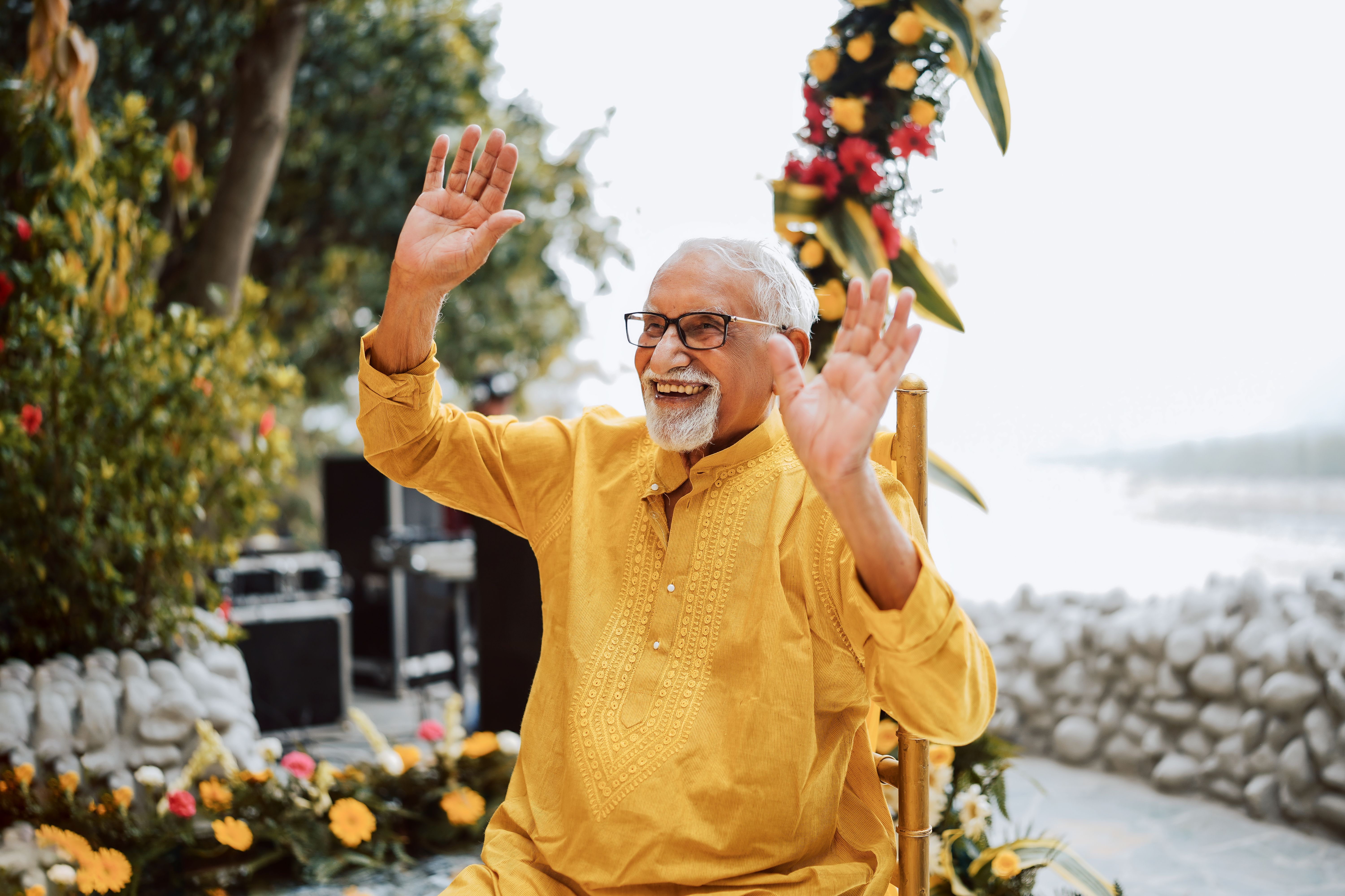 Happy senior man in traditional attire celebrating outdoors with lifted hands and a bright smile.