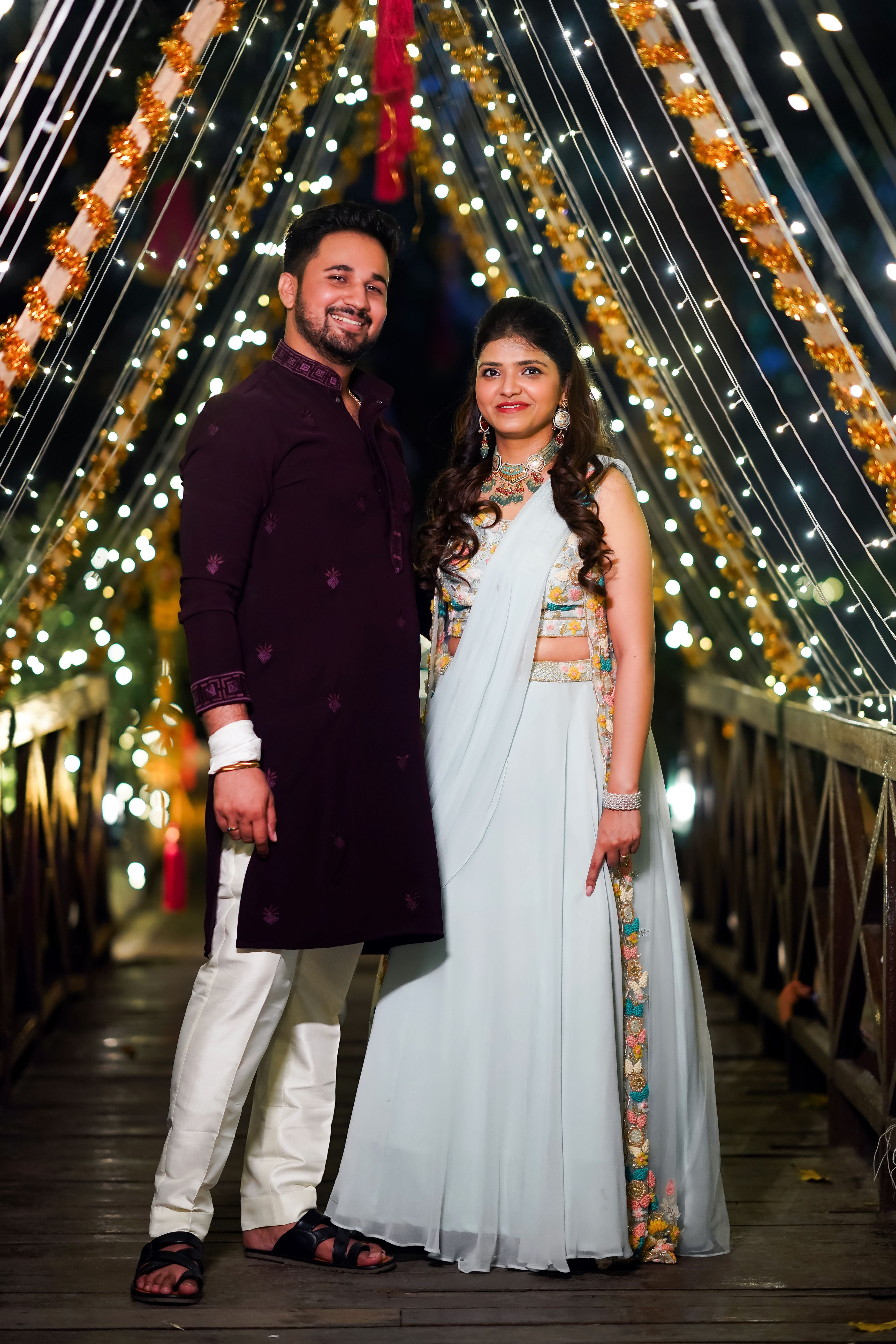 A couple in traditional attire poses on a beautifully illuminated bridge during nighttime festivities.