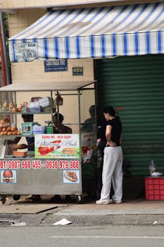 A street vendor in Vietnam serving banh mi to a customer at a food cart.