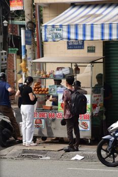 Customers purchase snacks from a bustling street food stall under a striped awning.