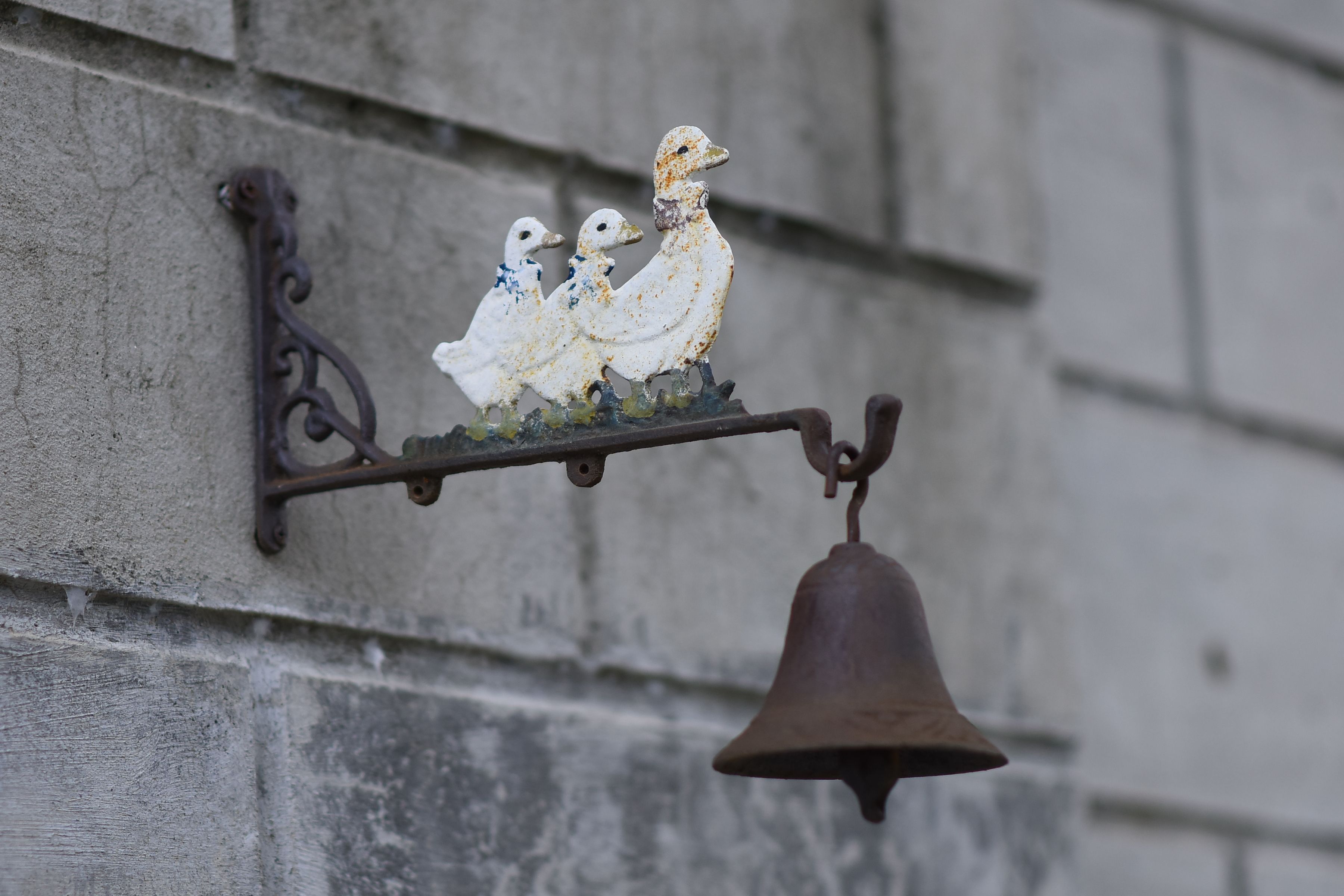 A vintage metal bell featuring an intricate duck figurine on a rustic wall. Perfect for decor enthusiasts.