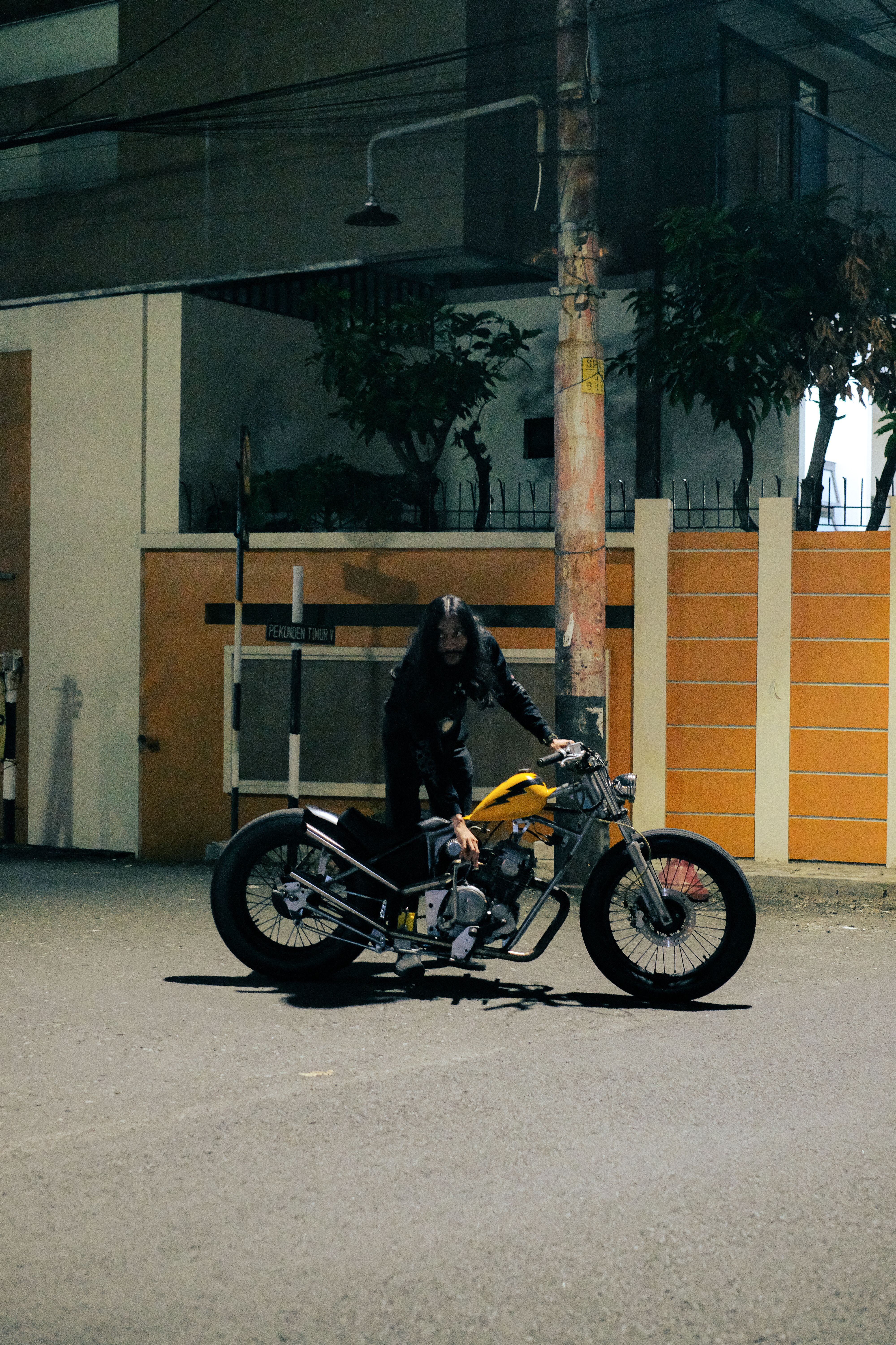 A person with a custom vintage motorcycle on a quiet city street at night.