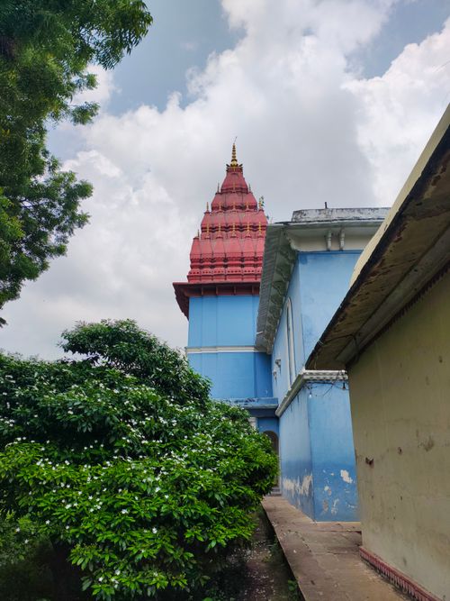 Free A vibrant Hindu temple tower surrounded by lush greenery under a cloudy sky. Stock Photo