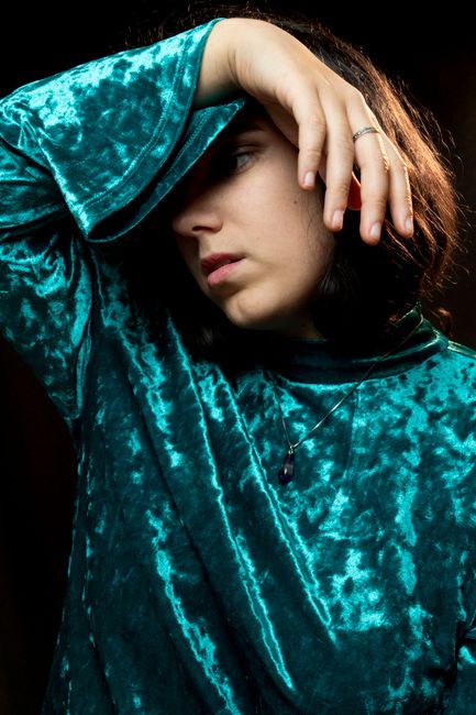 Velvet fashion portrait, woman posing with hand on forehead, studio photography.