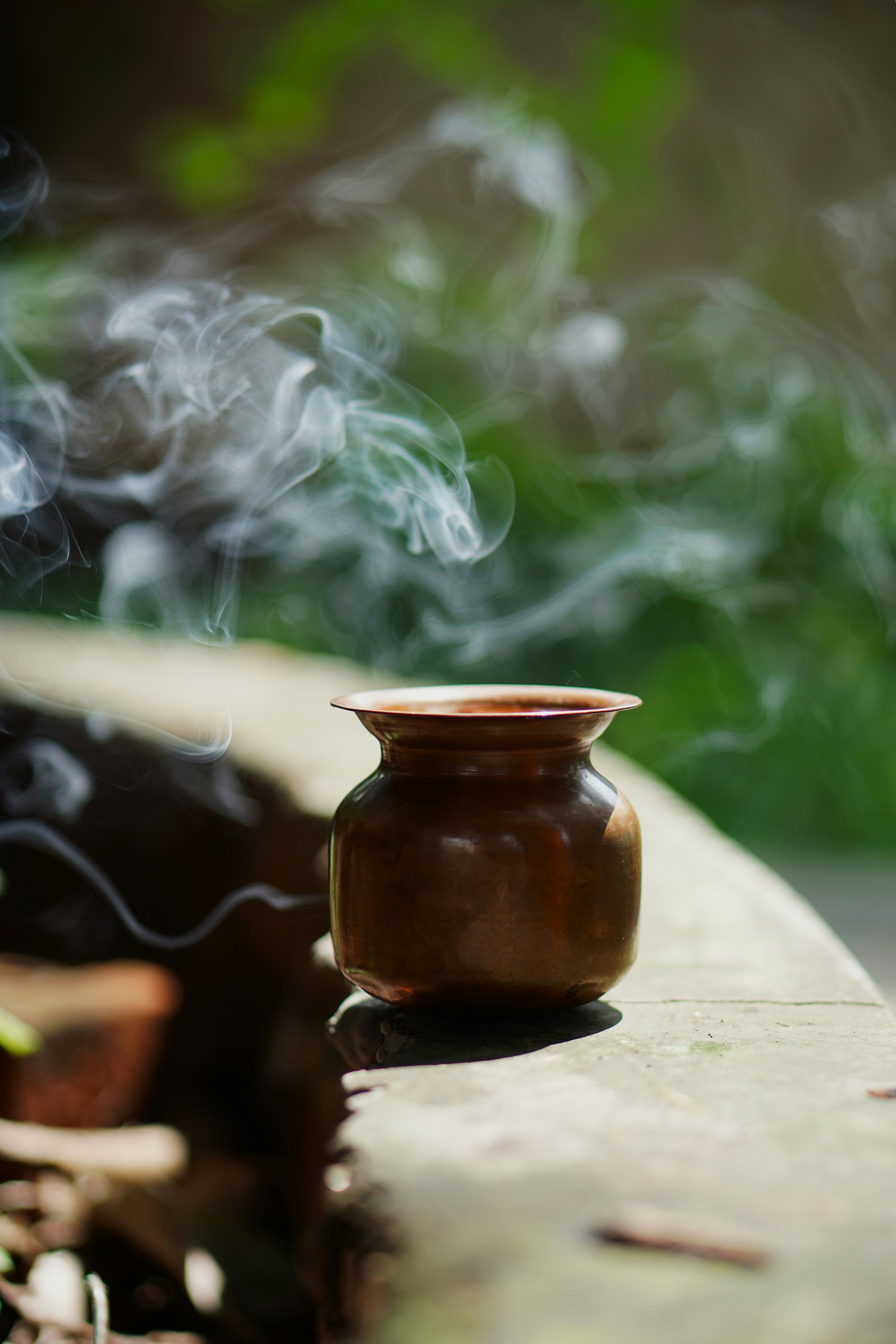 A copper pot with incense smoke creating a serene outdoor ambiance in natural sunlight.