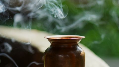 A copper pot with incense smoke creating a serene outdoor ambiance in natural sunlight.