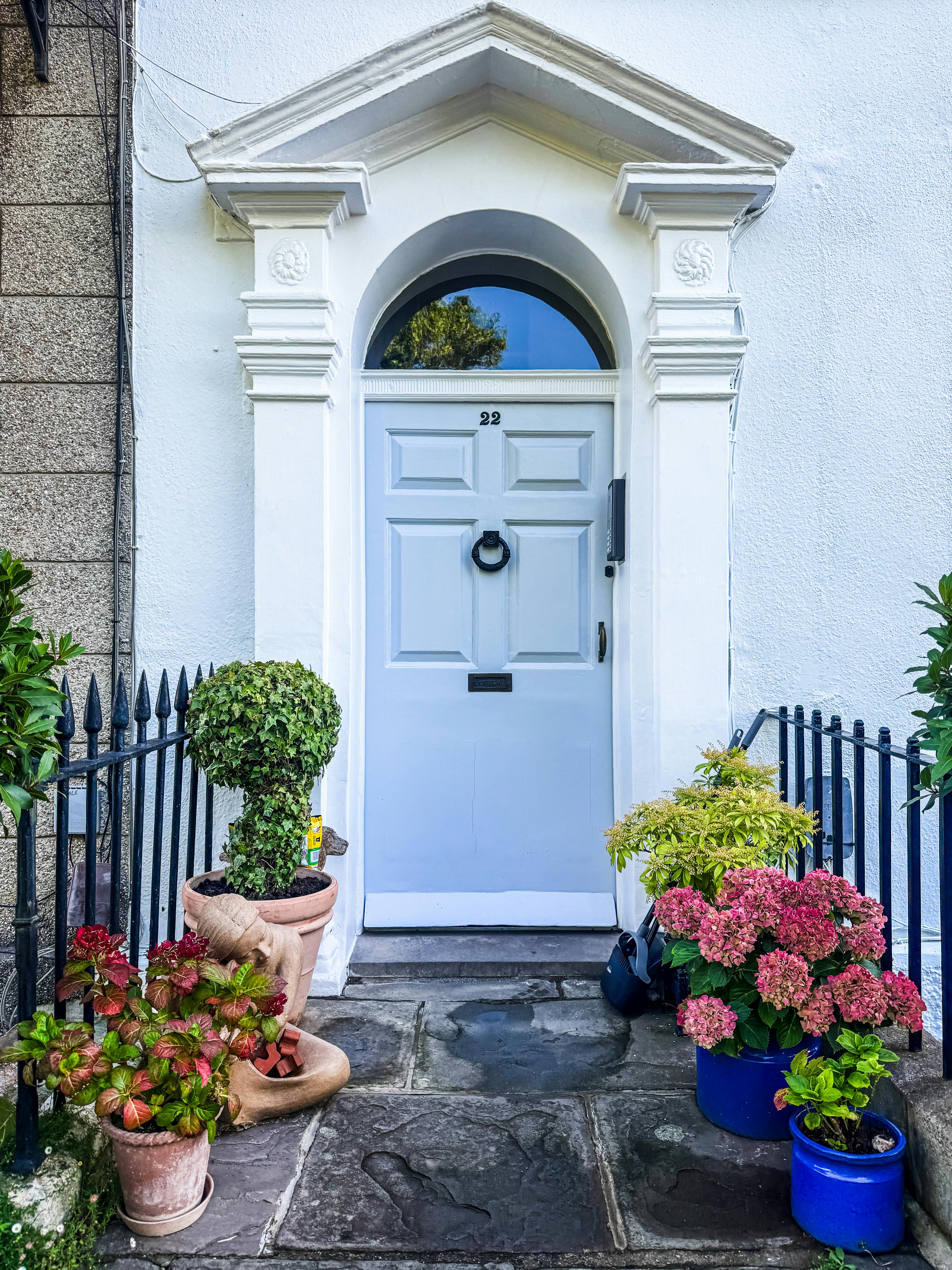 Elegant Georgian doorway in England adorned with vibrant potted flowers.