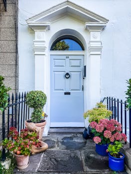 Elegant Georgian doorway in England adorned with vibrant potted flowers.