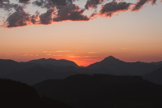 A tranquil view of mountain silhouettes against a vibrant sunset sky with clouds.