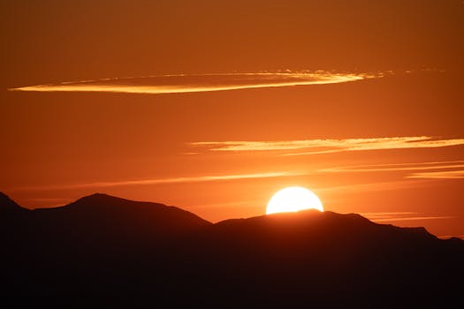 Beautiful sunrise casting an orange glow over silhouetted mountain peaks, creating a tranquil scene.