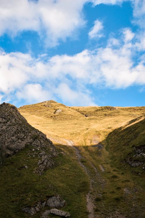 Free Lush hiking path between hills under a cloudy blue sky in England. Stock Photo