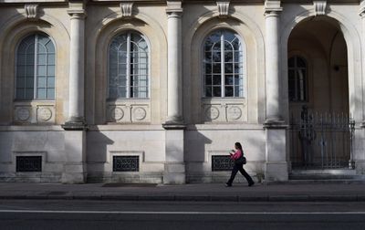 Une femme marche sur le trottoir à côté d'un bâtiment historique à Nancy, Grand Est, France.