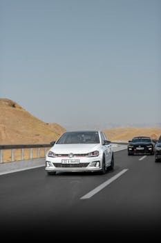 A white car driving on a desert highway with a clear blue sky, showcasing road trip adventure.