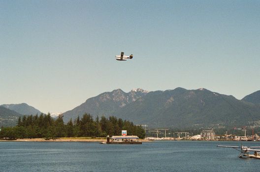 Seaplane flying above Vancouver Harbor with scenic mountain backdrop on a clear day.