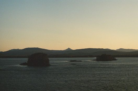 Peaceful island view during sunset with calm waters and mountainous horizon.