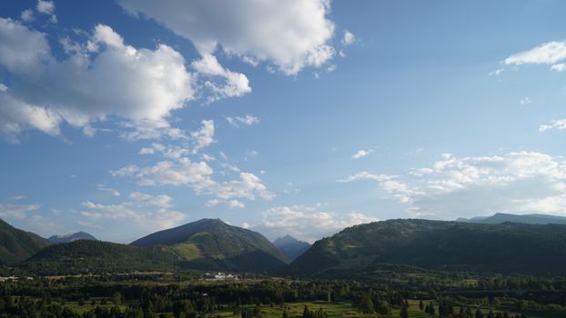 Serene mountain landscape with lush greenery under a clear blue sky with clouds.