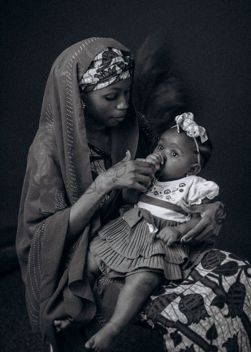 Free African mother lovingly holds her baby, both in traditional attire, showcasing Nigerian culture. Stock Photo