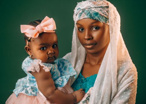 Free A mother lovingly holds her baby, both dressed in vibrant traditional Nigerian attire. Stock Photo