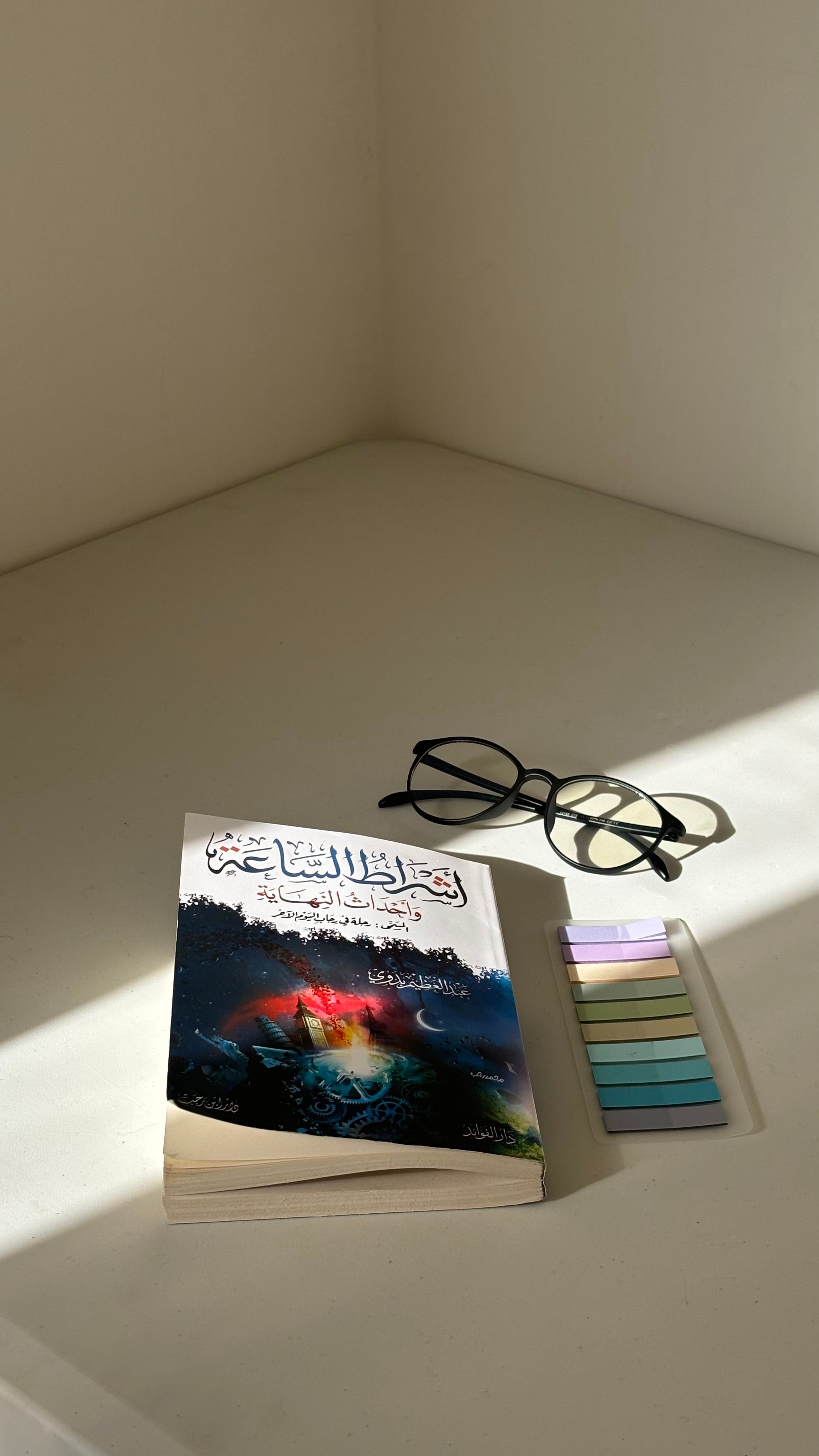 A book, reading glasses, and bookmarks on a table in soft daylight.