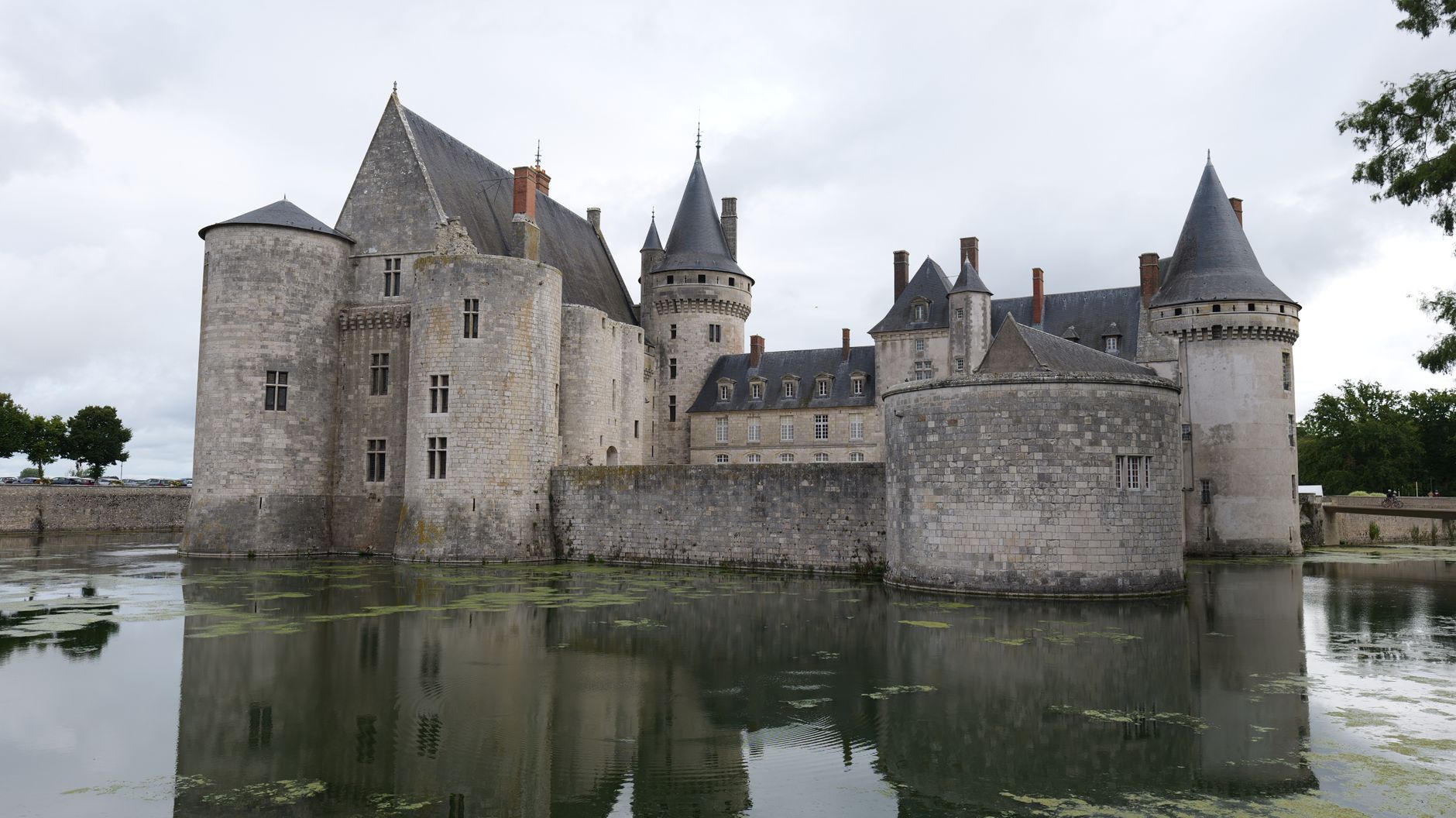 Majestic view of Château de Sully-sur-Loire in France with reflection in moat under cloudy skies.