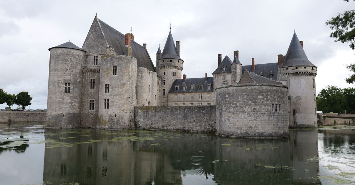 Majestic view of Château de Sully-sur-Loire in France with reflection in moat under cloudy skies.