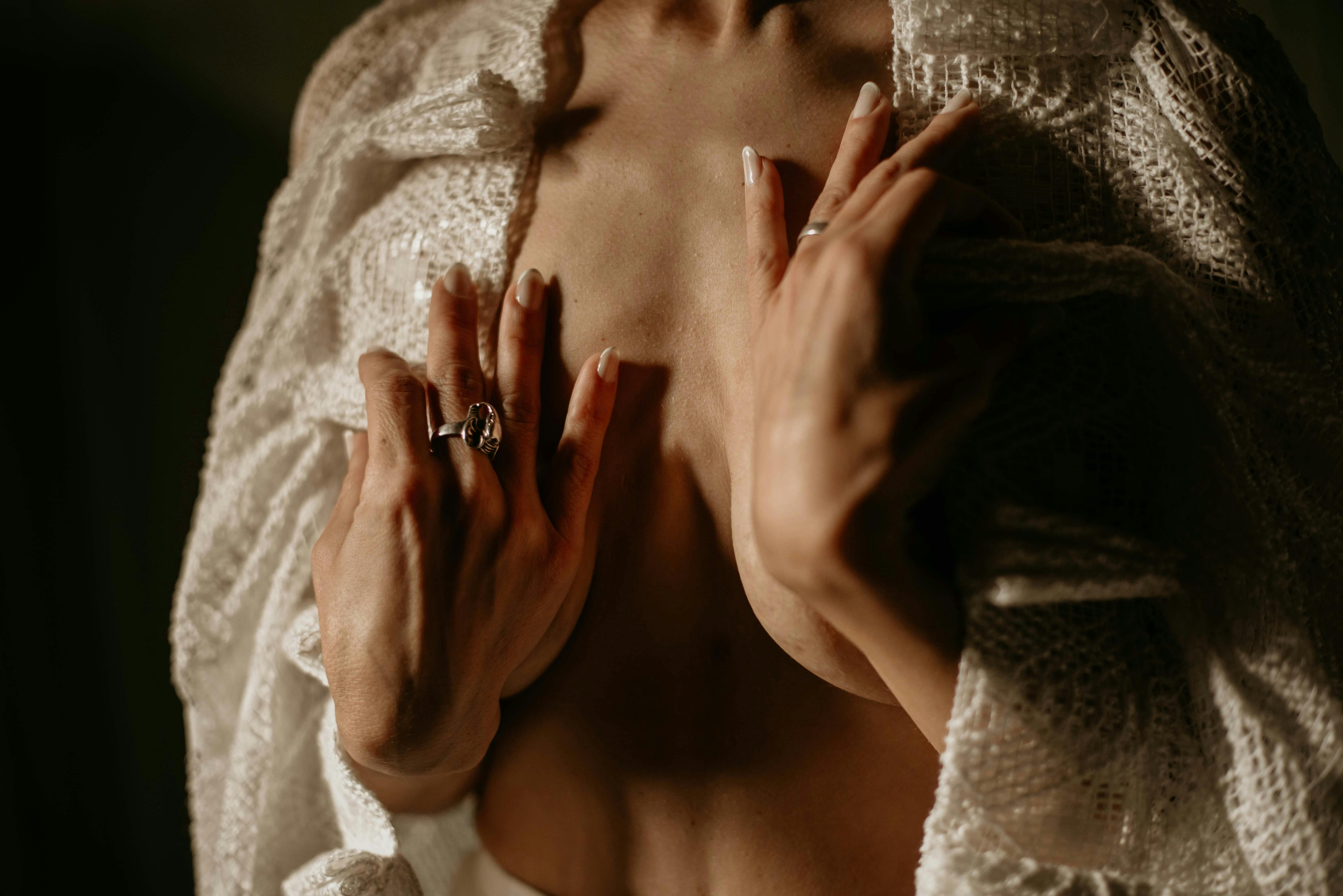 A close-up portrait of a woman's hands on her chest, wrapped in a cozy sweater.