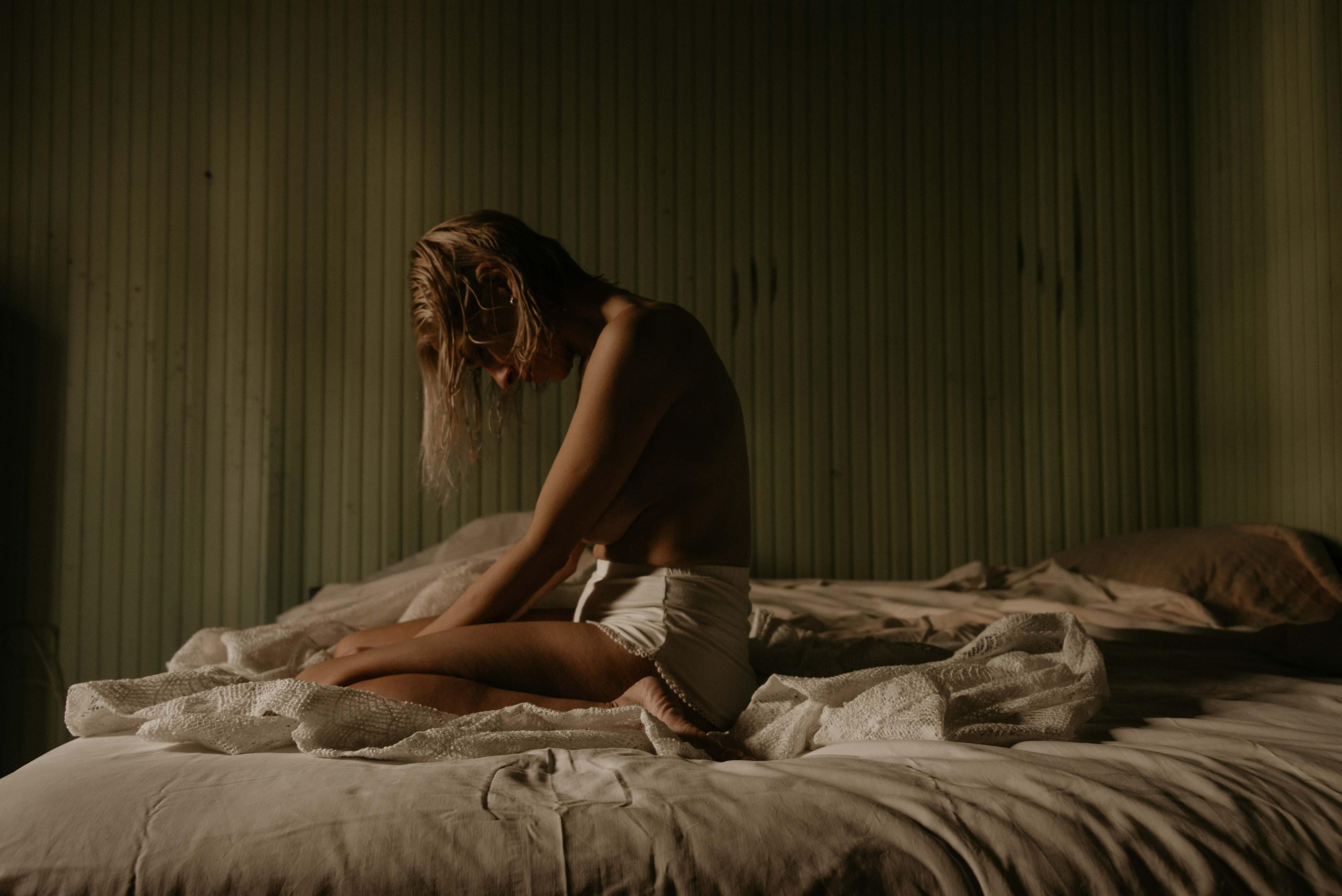 Person sitting contemplatively on a bed in soft bedroom light
