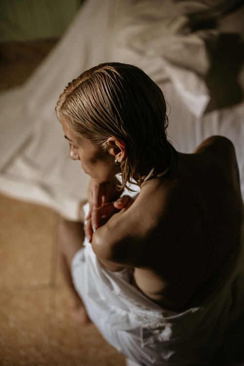Free A dramatic artistic portrait of a woman wrapped in a sheet, with wet hair, captured in warm, soft lighting from above. Stock Photo