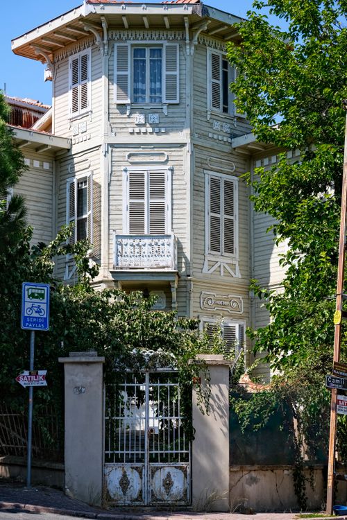 Free Victorian-style house surrounded by lush greenery and street signs, showcasing architectural beauty. Stock Photo