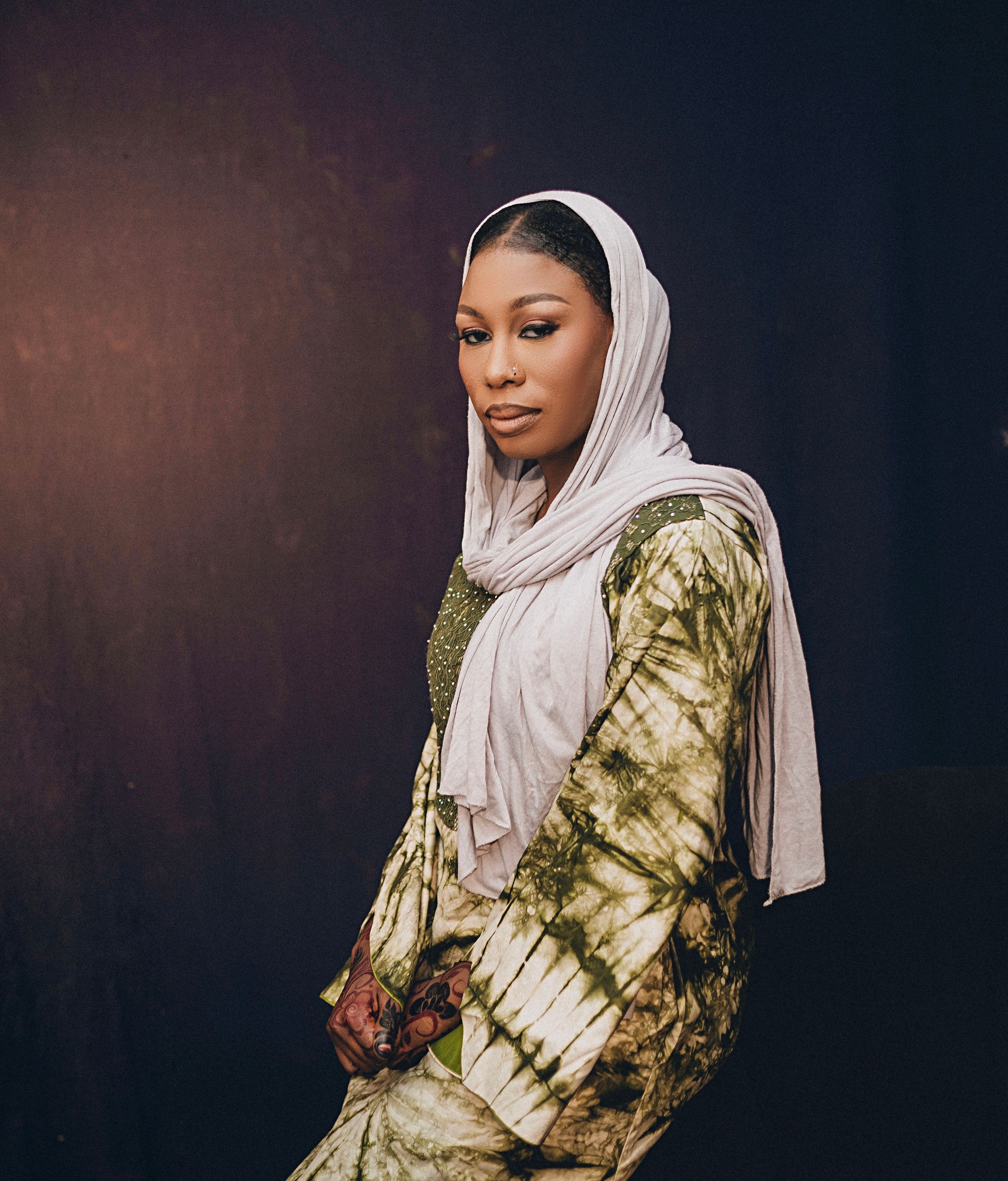 Portrait of a woman in tie-dye dress and headscarf against dark background.