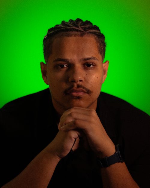 Free Serious portrait of a man with folded hands against a vibrant green backdrop, evoking focus and contemplation. Stock Photo
